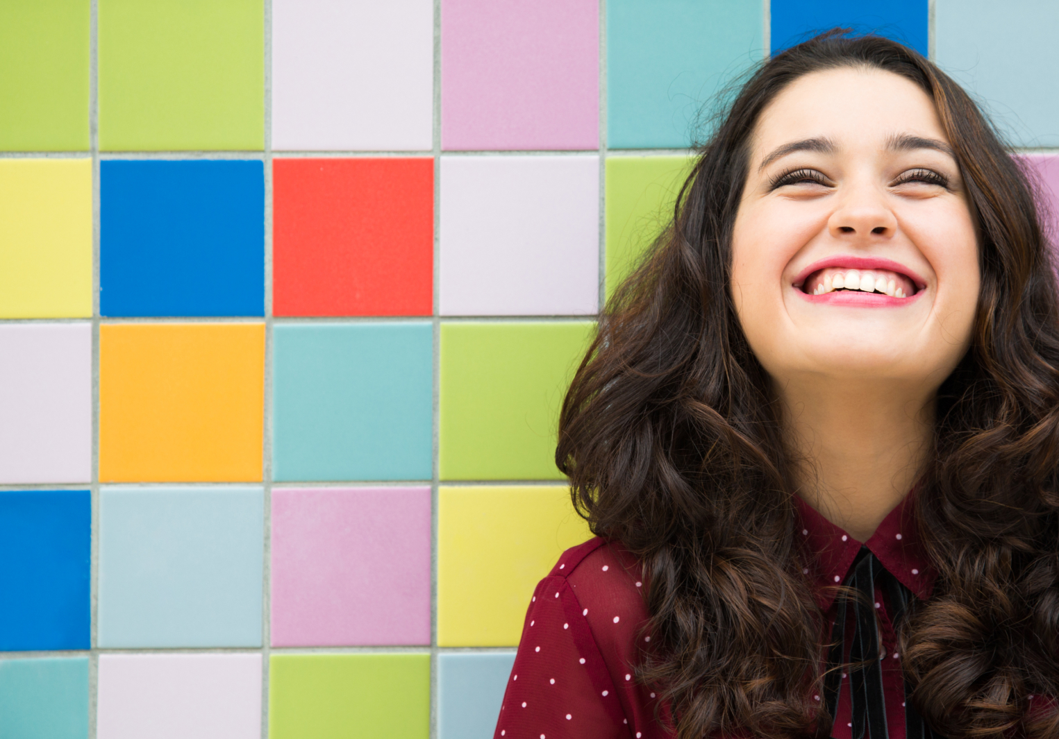 Young woman smiling leaning her head back against a wall of colourful square tiles
