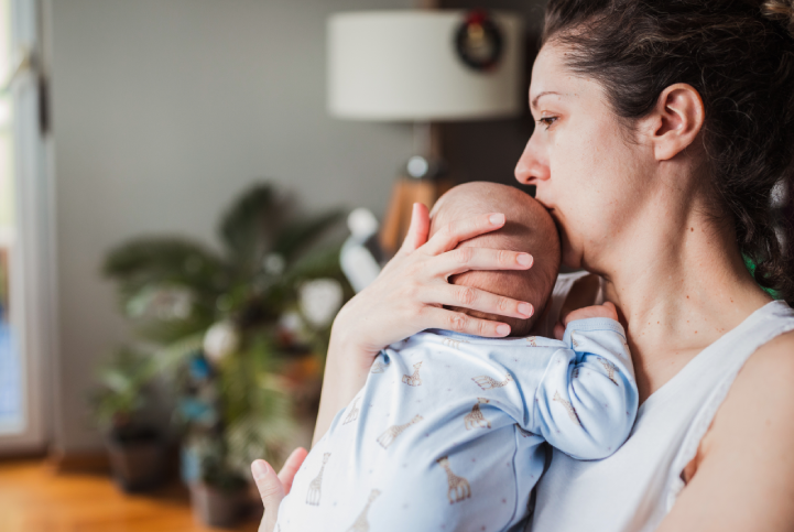 Mother lovingly holds their baby in their arms. The mother seems a bit sad. 