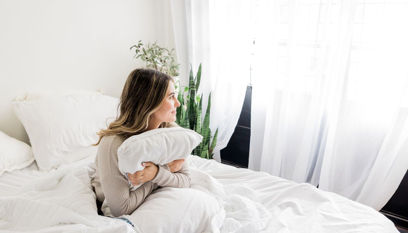 Young woman sits on her bed holding her pillow.