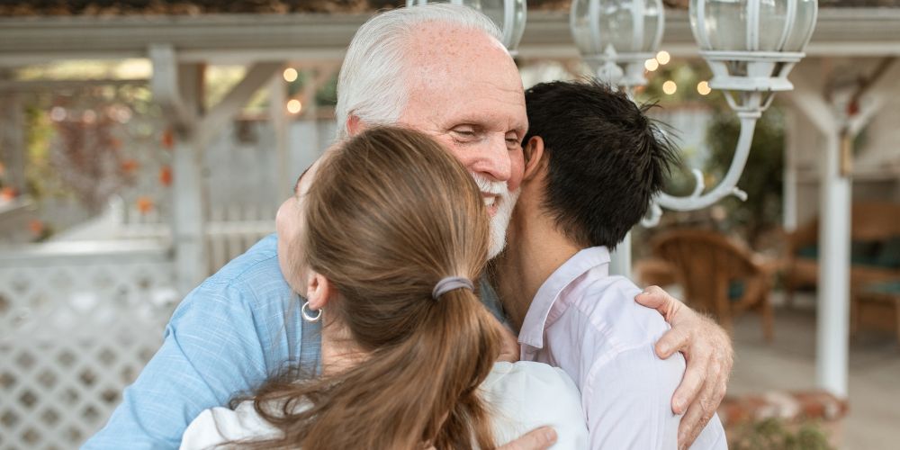 Older father hugging his two adult children