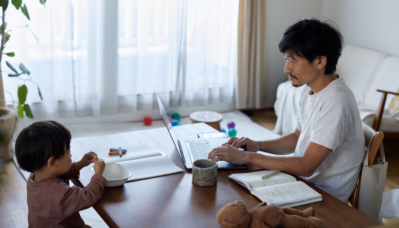 Father works on his laptop while his son plays.