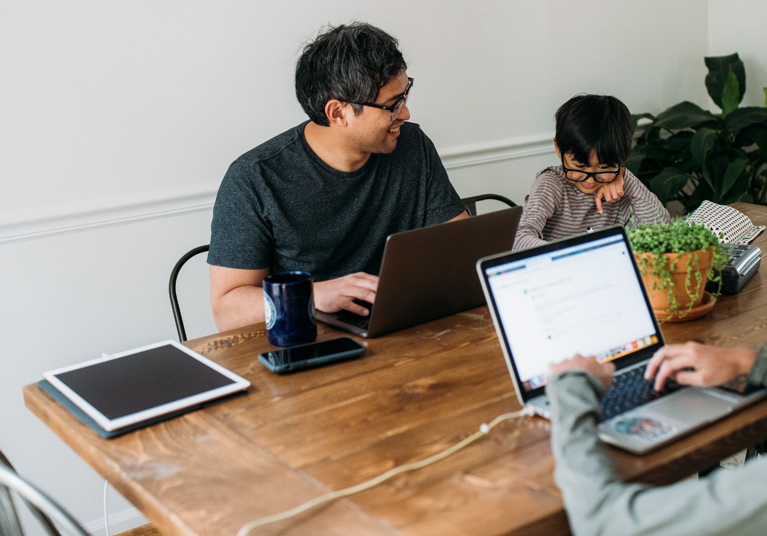 A dad sits at the table with his two sons, all working on laptops and talking