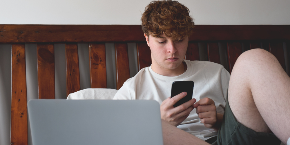 Young man looking over his phone while in bed