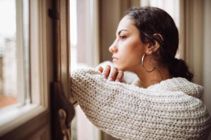 Pensive woman sitting by and looking out the window. 