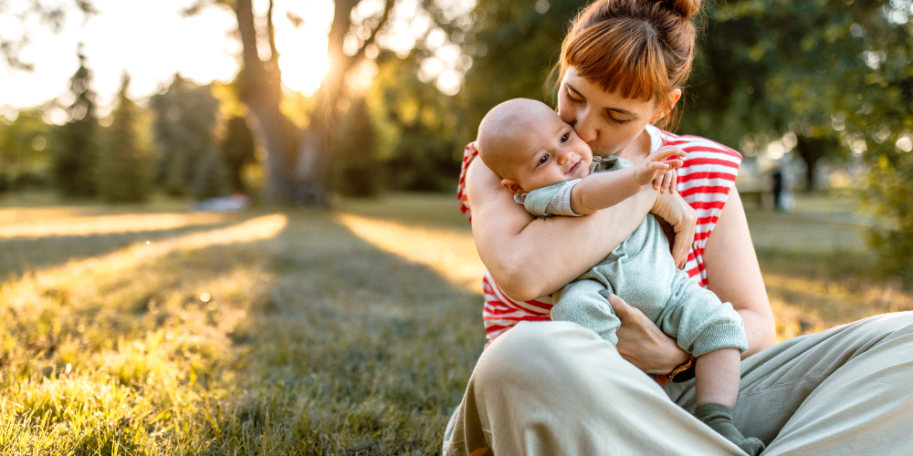 Woman kissing her baby on the cheek as they sit in the grass.