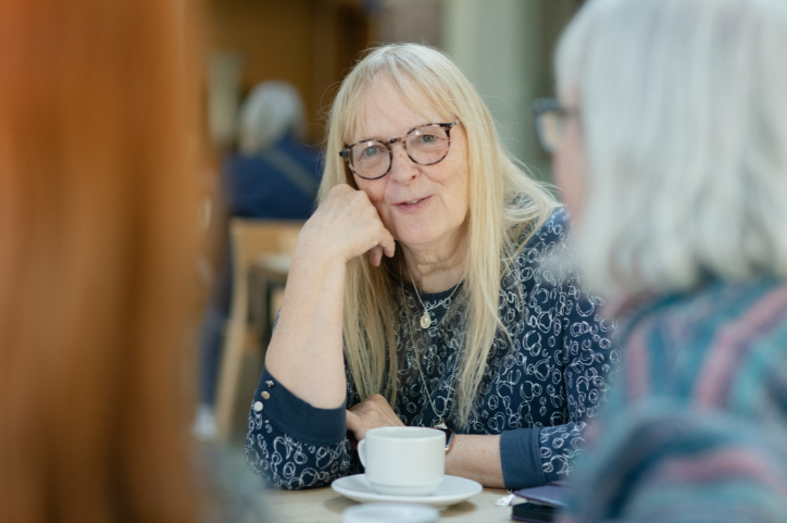 Older woman talking to her friends at a cafe. Both friends are blurred in the foreground.