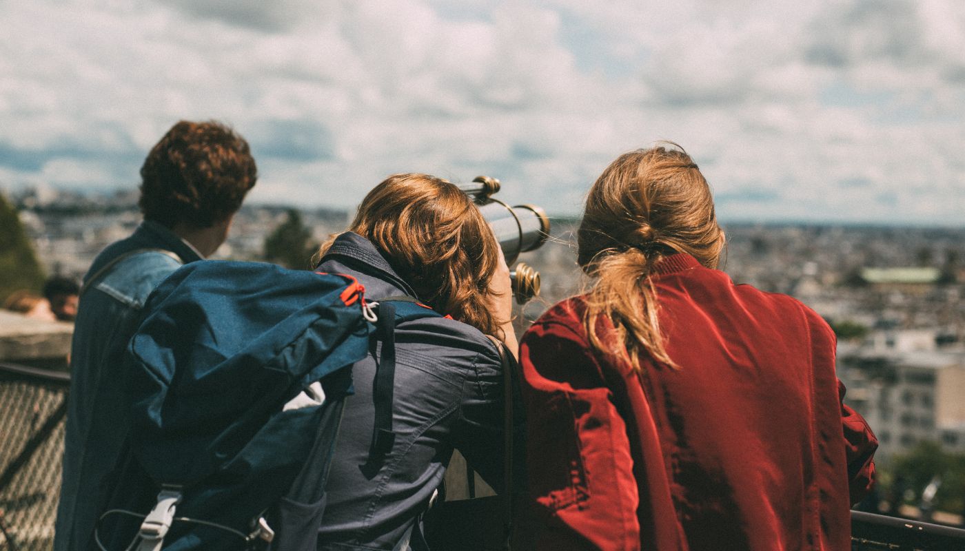 Three young people looking through a telescope over a city.