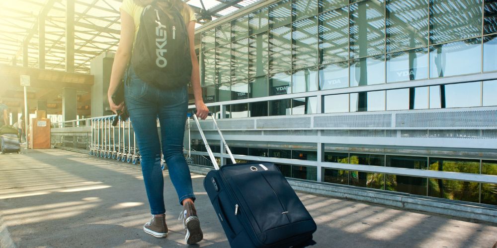 Young woman walking into airport wheeling suitcase