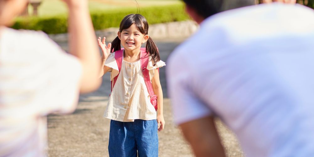 Young girl waving goodbye to her parents