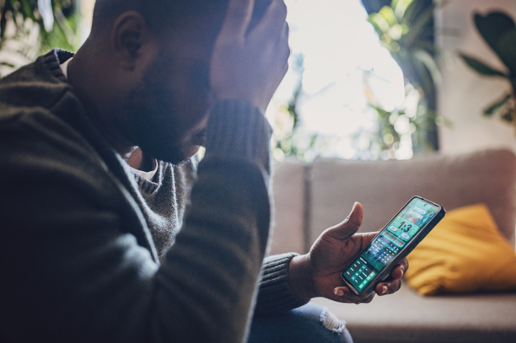 A man sitting with his head in his right hand and a phone open to a betting app in his left hand