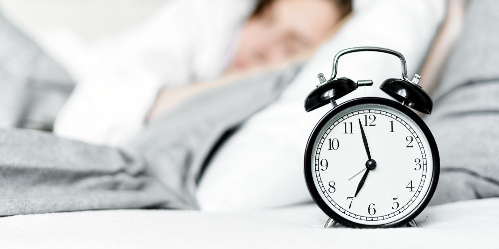 Person sleeping next to alarm clock